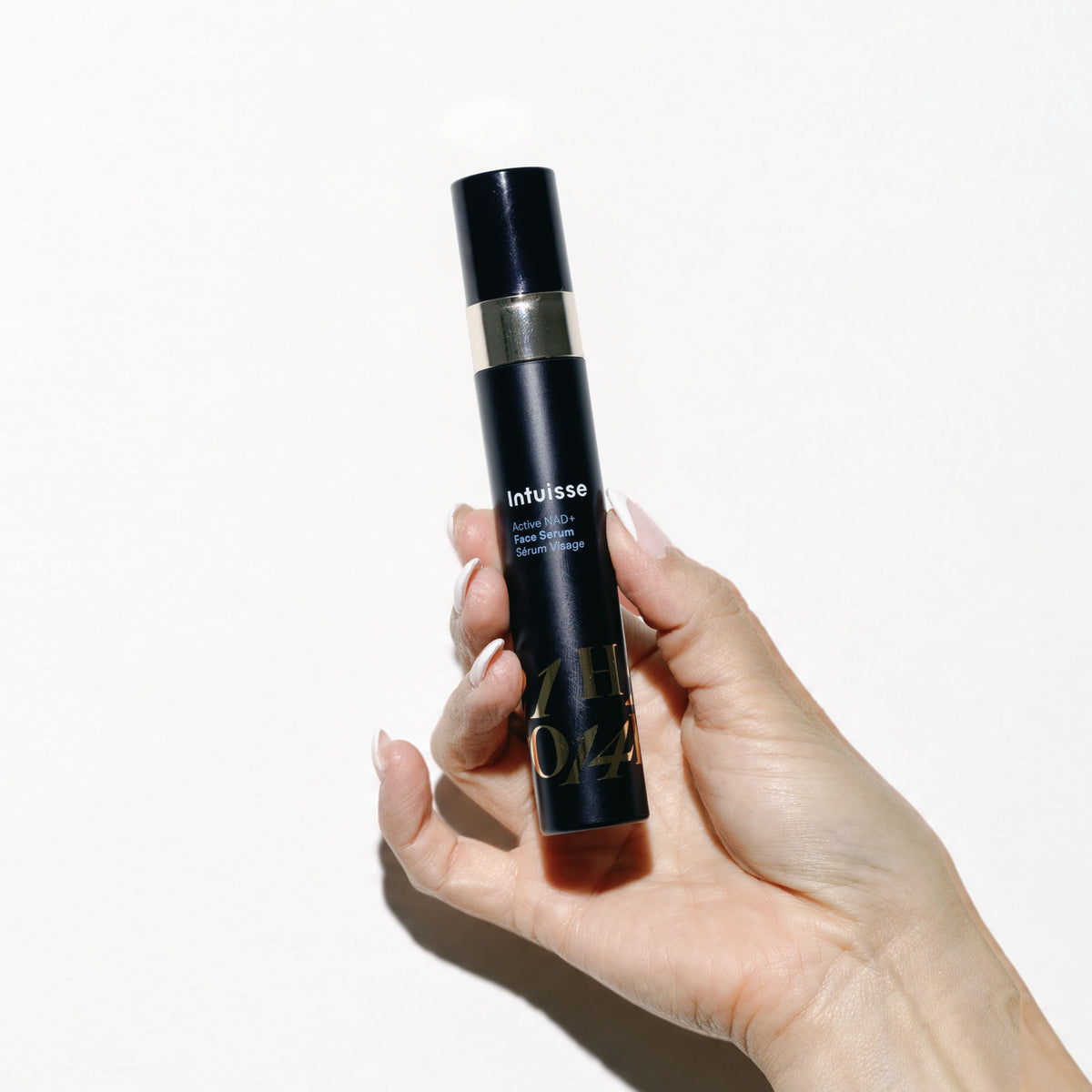 Hand holding the Intuisse Active NAD+ Face Serum against a white background.